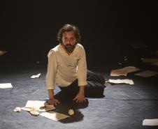 ator sentado no chão ao lado de diversos papeis