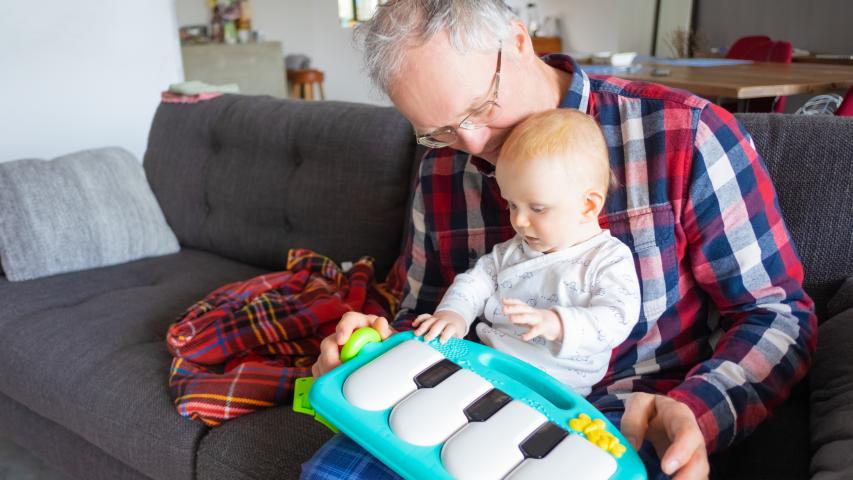 Homem brincando com bebê no colo e um piano de brinquedo
