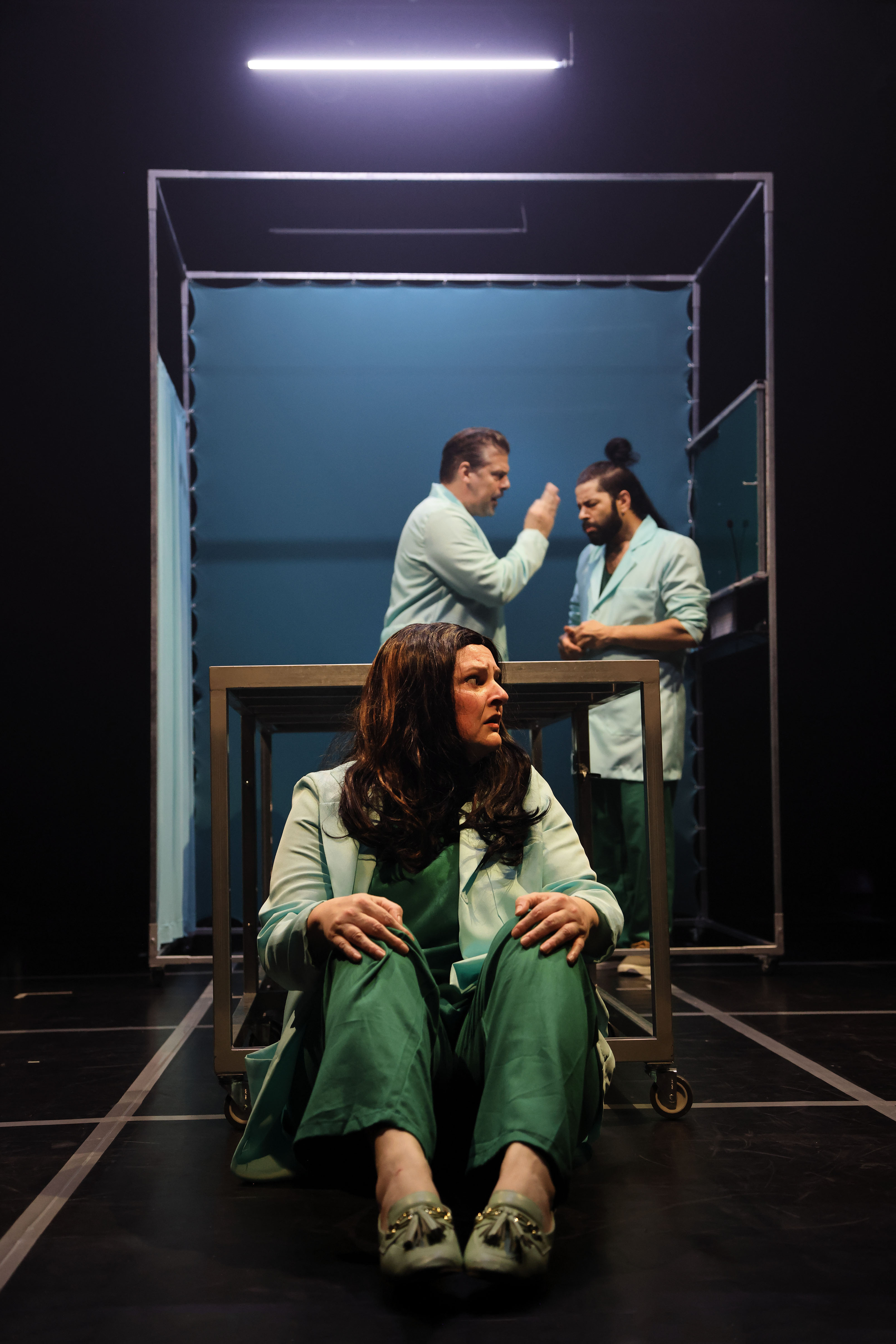 Cenas do espetáculo, com atores vestidos de médicos e uma paciente em cenário de sala de cirurgia