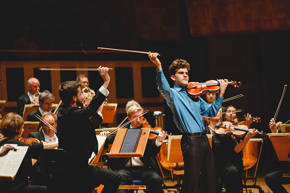 Solista vestido com camisa azul em apresentação com Orquestra.