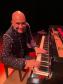 Rogério Koury sorrindo para a foto à frente de um piano