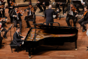 pianista sentado em frente ao piano, orquestra ao fundo