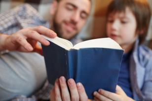 Foto de um pai lendo um livro de capa azul com seu filho