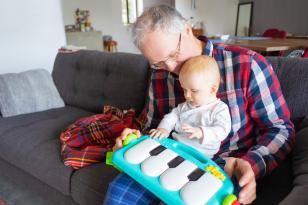 Homem brincando com bebê no colo e um piano de brinquedo