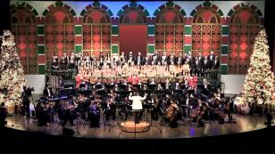 Foto de uma orquestra e coral se apresentando em um palco com decorações natalinas