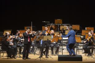 Foto de um maestro regendo dois violinistas durante um concerto