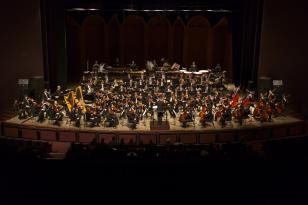 Foto dos músicos da Orquestra tocando seus instrumentos no palco do Guairão