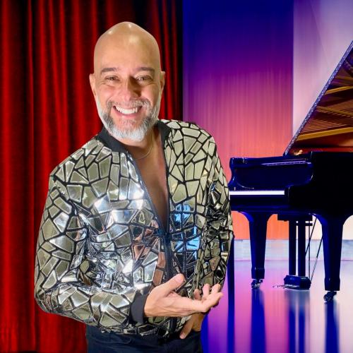 Pianista em primeiro plano com jaqueta brilhante; piano ao fundo do palco.