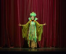 Ator Ranieri Gonzalez com a roupa verde do Senhor das Lendas de pé no paco do Guaíra. Ao fundo a cortina vermelha.