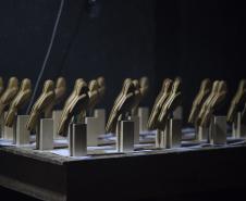 A premiação da edição anterior no placo do auditório Guairão e os troféus que os premiados vão receber, em formato de gralha azul, ave símbolo do Paraná. 