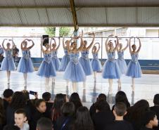 Grupo de dança se apresenta aos alunos no pátio da escola. As bailarinas vestem roupas na cor azul clara. 