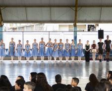 Grupo de dança se apresenta aos alunos no pátio da escola. As bailarinas vestem roupas na cor azul clara. 