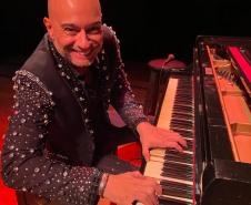 Rogério Koury sorrindo para a foto à frente de um piano