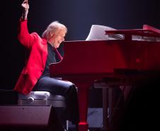 Richard Clayderman com terno vermelho em frente a um piano 