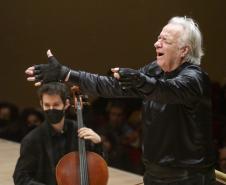 maestro, com camisa e luvas pretas, regendo orquestra