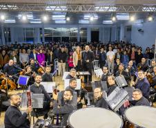 orquestra olha para camera ao fundo do palco. imagem também pega o publico que assistia