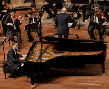 pianista sentado em frente ao piano, orquestra ao fundo
