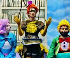 Personagens Ritinha, Doroteia e Nico em frente a uma prateleira da biblioteca