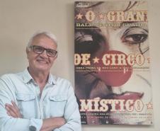 Gilberto Carbonar, funcionário mais antigo do Teatro Guaíra, em atividade há 49 anos, posando ao lado do cartaz de divulgação de “O Grande Circo Místico”