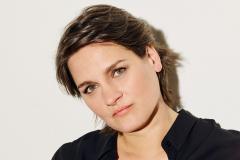 Madeleine em ensaio fotográfico. A cantora está de preto em frente a um fundo branco, olhando para a foto.