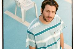 Tiago Nacarato à frente da imagem, com uma cadeira no fundo em um ambiente azul