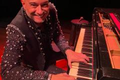 Rogério Koury sorrindo para a foto à frente de um piano