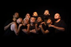 Grupo teatral abraçado sob fundo preto