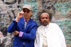 Chico César e Zeca Baleiro em imagem de divulgação do novo álbum "Ao Arrepio da Lei". Os artistas posam para foto em frente a uma parede com pinturas urbanas