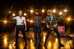 Tony Bellotto, Branco Mello, Sérgio Britto em cima do palco. Atrás, luzes amarelas diretas decoram o palco