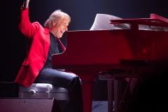 O pianista no palco em posição de tocar o piano, com o braço direito erguido em pose alegre.