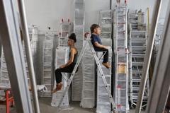 atores sentados de costas um para o outro em uma escada de serviço em uma sala com várias escadas iguais