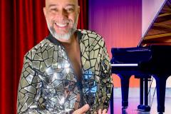 Pianista em primeiro plano com jaqueta brilhante; piano ao fundo do palco.