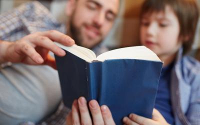 Foto de um pai lendo um livro de capa azul com seu filho