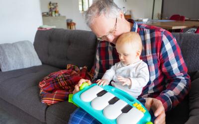 Homem brincando com bebê no colo e um piano de brinquedo