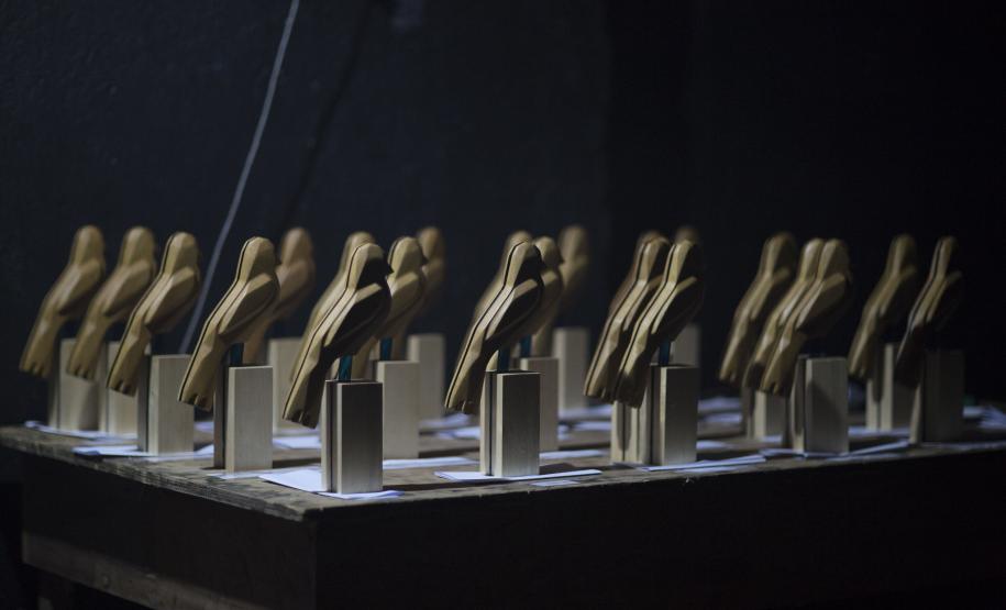 A premiação da edição anterior no placo do auditório Guairão e os troféus que os premiados vão receber, em formato de gralha azul, ave símbolo do Paraná.