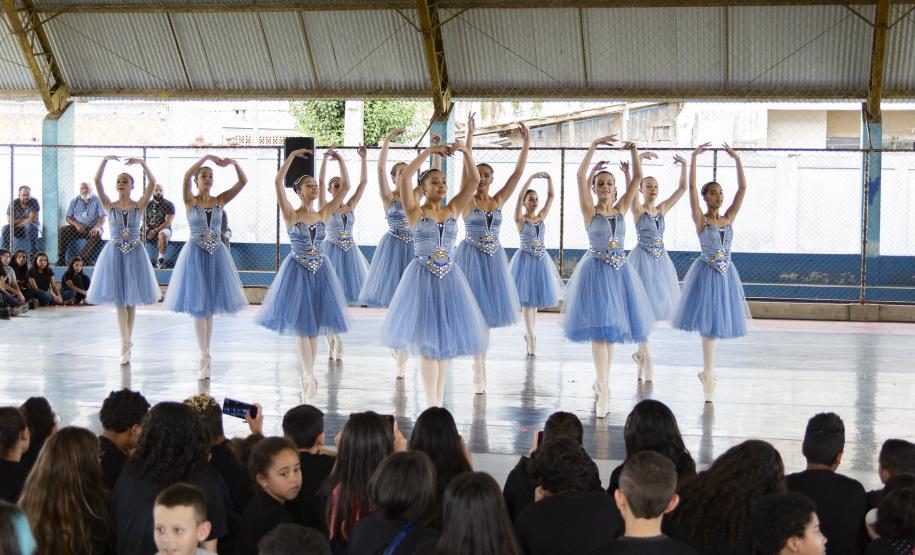 Grupo de dança se apresenta aos alunos no pátio da escola. As bailarinas vestem roupas na cor azul clara.