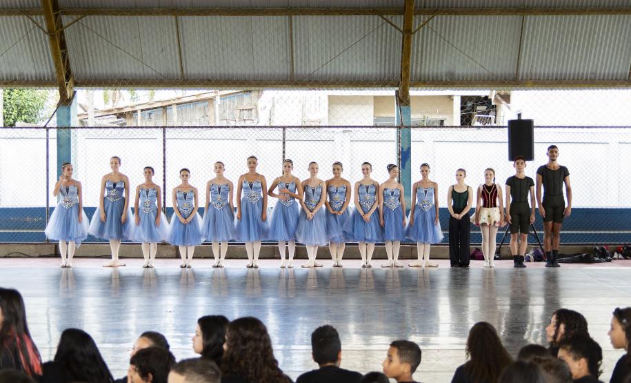 Grupo de dança se apresenta aos alunos no pátio da escola. As bailarinas vestem roupas na cor azul clara.