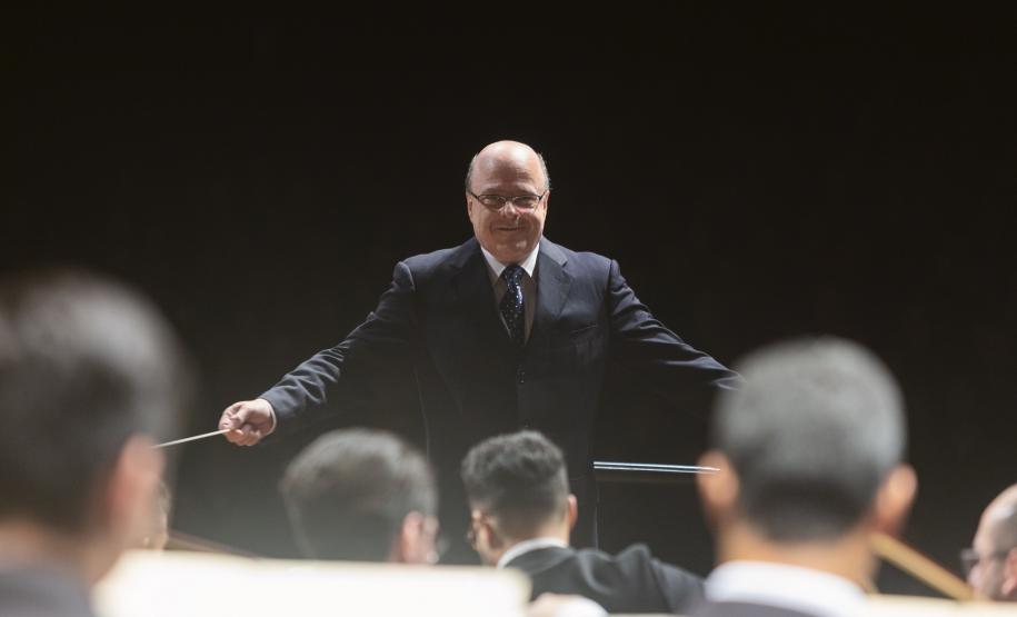 Toda a orquestra, com seus instrumentos, o coro, os solistas, os músicos convidados e o maestro estão posicionados durante o concerto no placo do Teatro Guaíra, com roupas de gala.