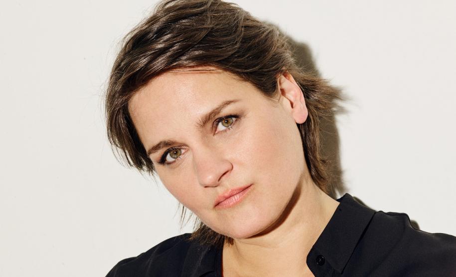 Madeleine em ensaio fotográfico. A cantora está de preto em frente a um fundo branco, olhando para a foto.