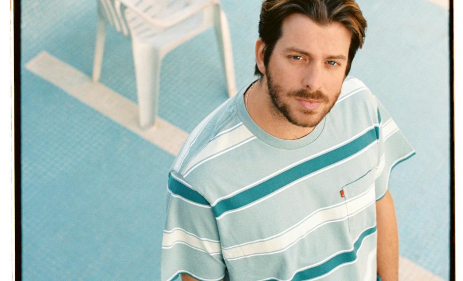 Tiago Nacarato à frente da imagem, com uma cadeira no fundo em um ambiente azul