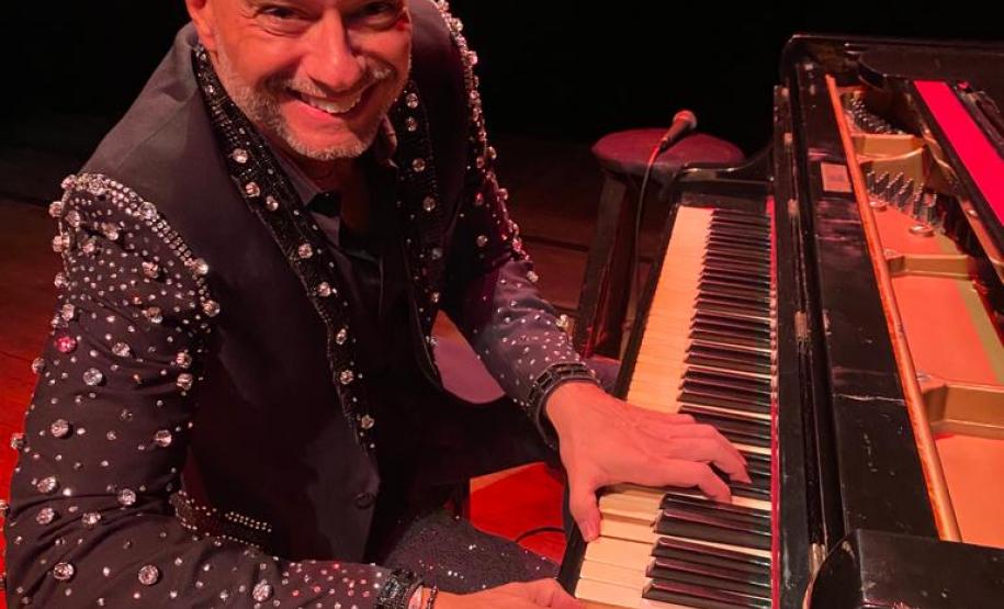 Rogério Koury sorrindo para a foto à frente de um piano