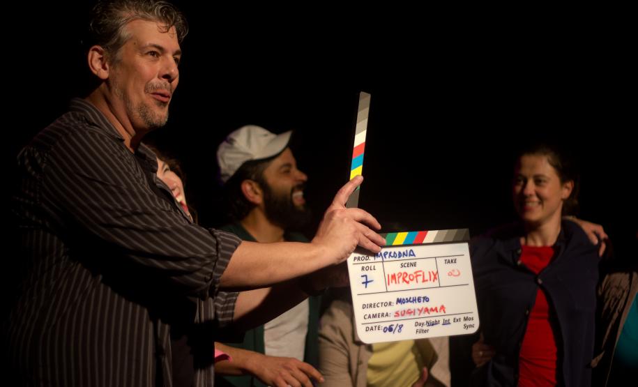 diretor com claquete em mãos e personagens ao fundo