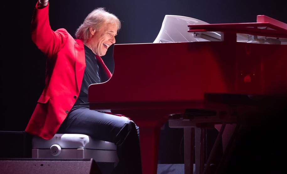 Richard Clayderman com terno vermelho em frente a um piano