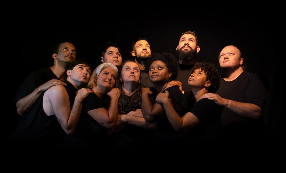 Grupo teatral abraçado sob fundo preto