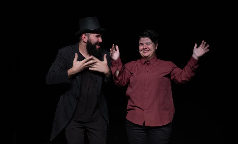 dois atores em cena sob fundo preto.