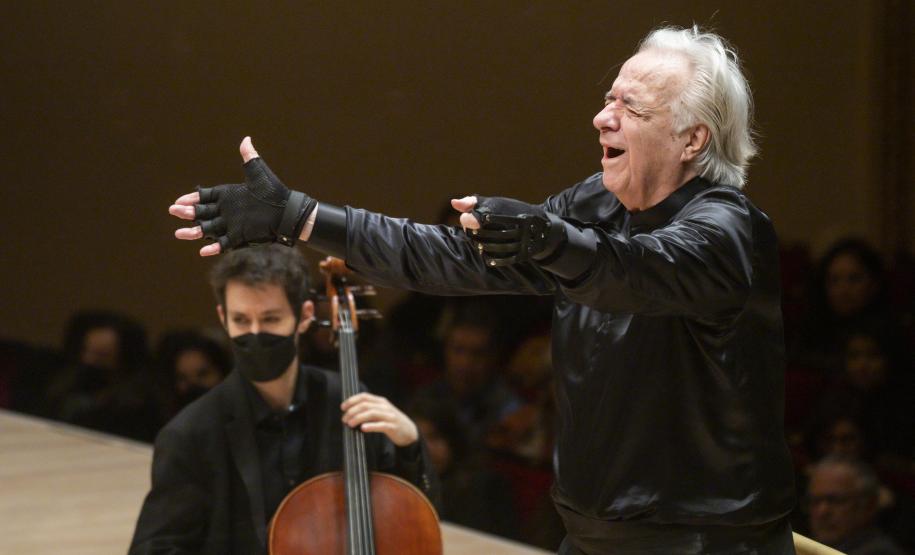 maestro, com camisa e luvas pretas, regendo orquestra