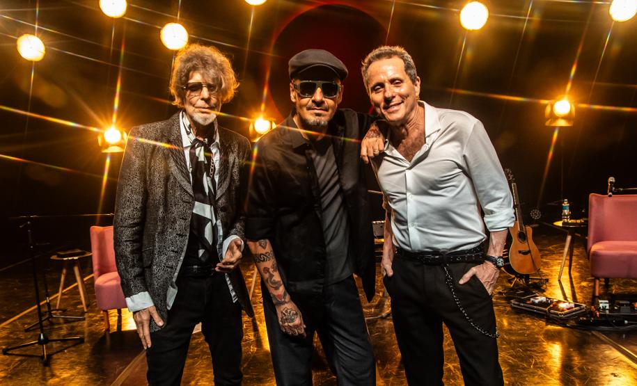 Tony Bellotto, Branco Mello, Sérgio Britto em cima do palco. Atrás, luzes amarelas diretas decoram o palco