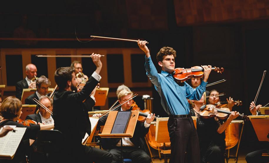 Solista vestido com camisa azul em apresentação com Orquestra.