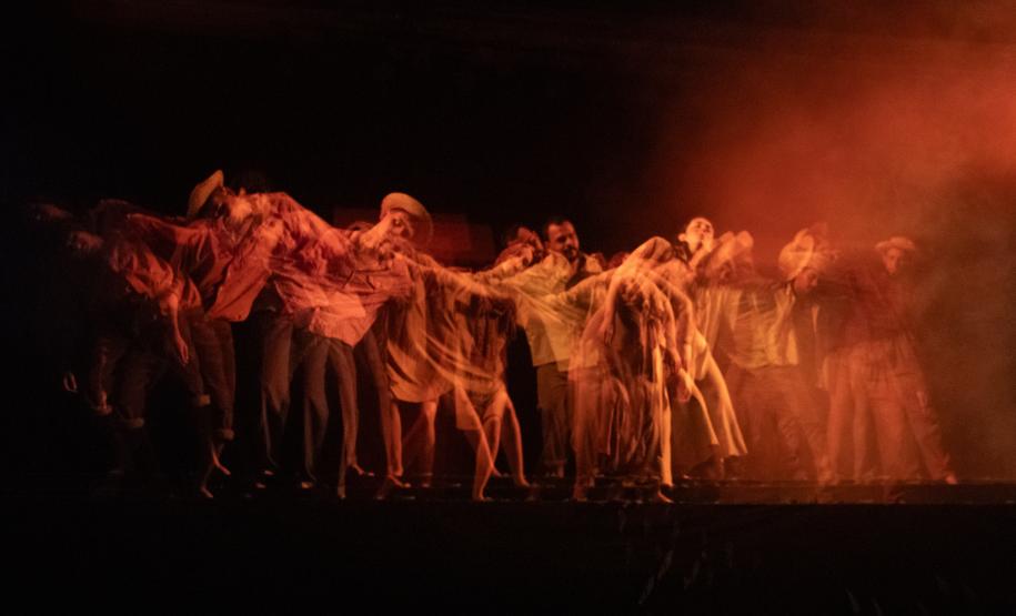 personagens em peça "Uma jornada no sertão", com luzes vermelhas e cenário típico regional