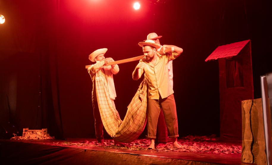 personagens em peça "Uma jornada no sertão", com luzes vermelhas e cenário típico regional